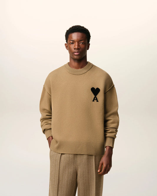 Man wearing a Ami De Coeur Crewneck Brown Wool Sweater UKS838.018.288 with a black heart and letter 'A' emblem on a white background