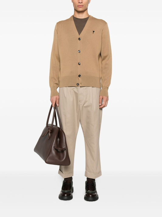 Person wearing a Wool Ami De Coeur Cardigan Camel/Black HKC361.001.288, brown pants, and holding a brown bag on a white background