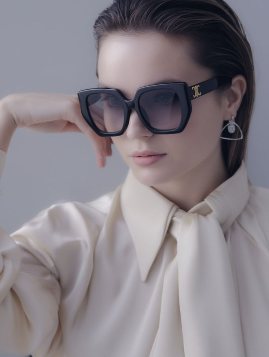 Woman wearing a beige blouse and Celine CL40239F 01F Butterfly Triomphe Sunglasses In Acetate with a gold logo, against a gray background