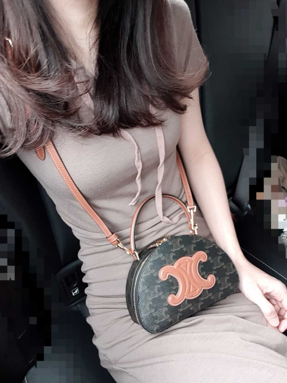 Woman holding a Celine Half Moon Case In Triomphe Canvas & Calfskin 10K642ECM.04LU with a distinctive logo, sitting in a vehicle.
