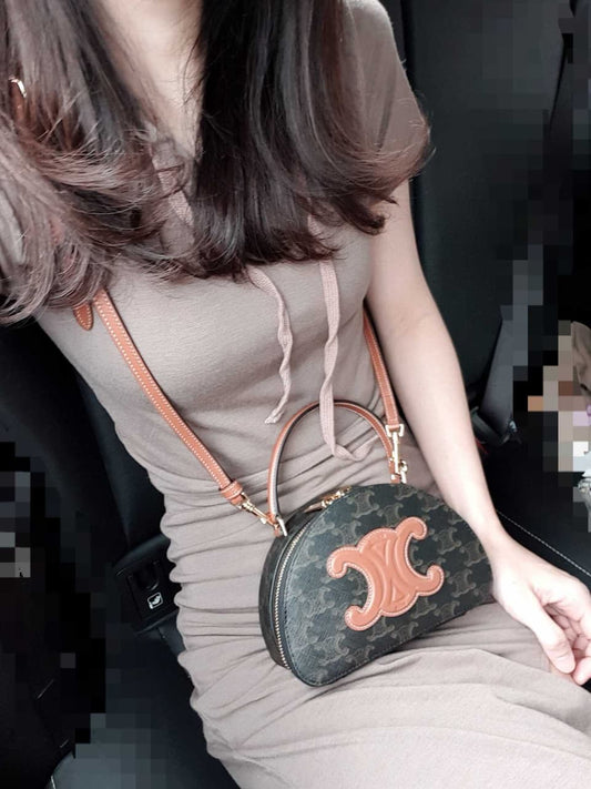 Woman holding a Celine Half Moon Case In Triomphe Canvas & Calfskin 10K642ECM.04LU with a distinctive logo, sitting in a vehicle.