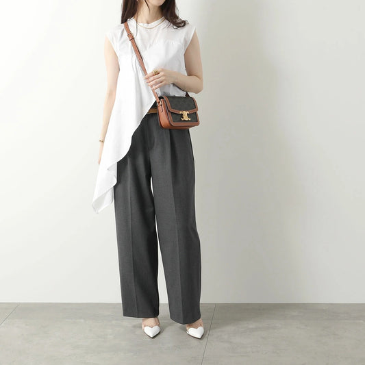 Woman wearing a white sleeveless top and gray wide-leg pants, holding a Celine Teen Triomphe Bag In Triomphe Canvas & Calfskin 188882BZ4.04LU against a plain background.