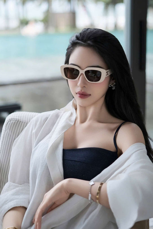 Woman wearing CELINE Triomphe 04 Sunglasses in Acetate Ivory CL40216U 25E and a light jacket sitting outdoors with a blurred background
