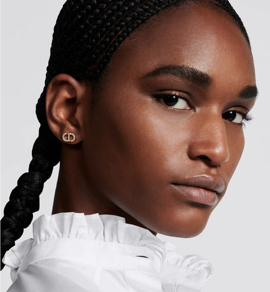 Close-up of a woman with braided hair wearing a Dior Petit CD Mini Stud Earrings Gold E3045WOMCY-D03S against a light gray background