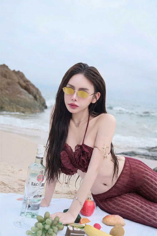 Woman wearing Fendi FE4075US 30L First Crystal Sunglasses Gold in maroon bikini sitting on a beach with a bottle and fruits.