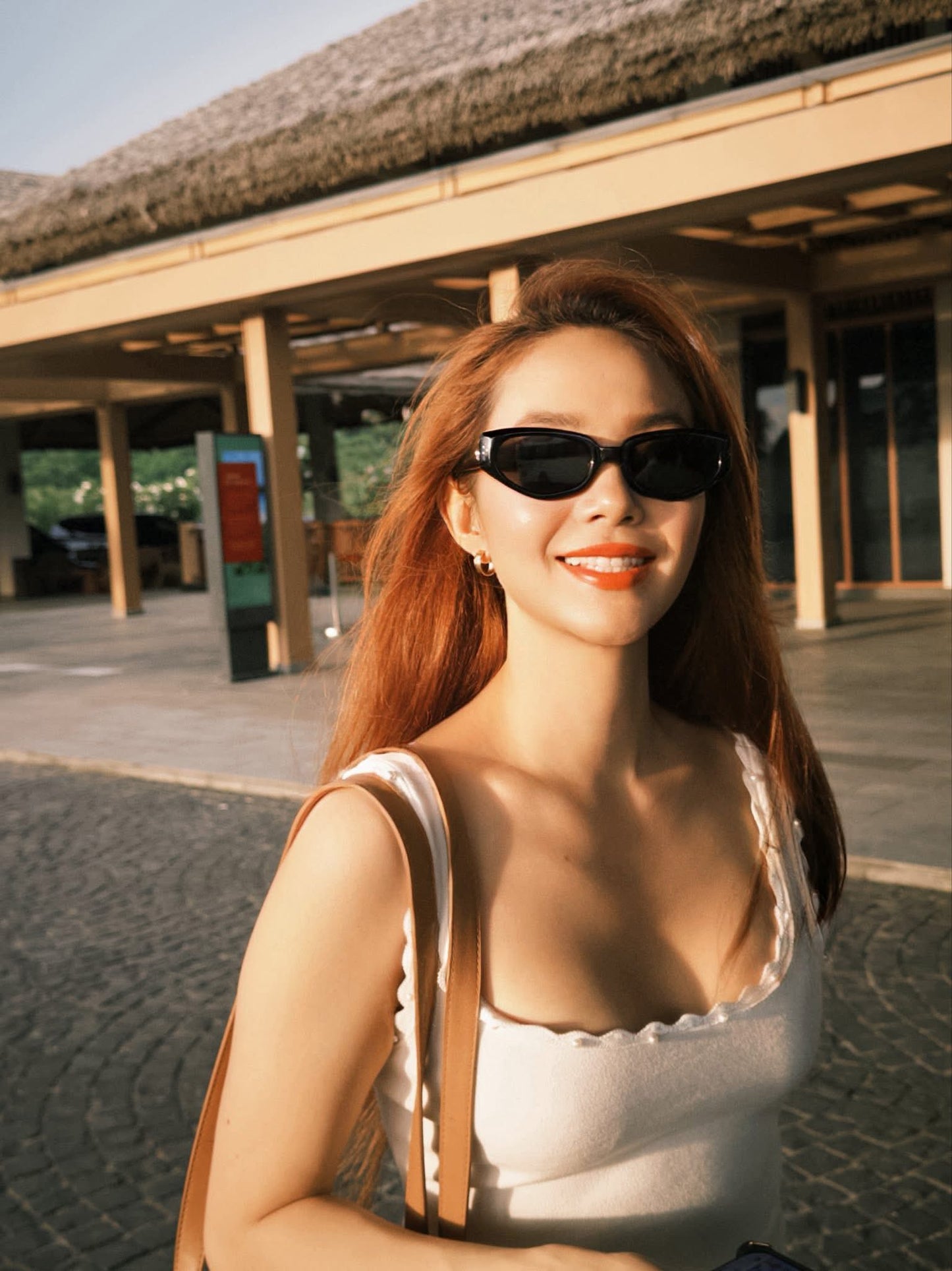 Woman wearing GENTLE MONSTER (GM) DEVON (01) and a white top with a brown bag, standing outdoors.