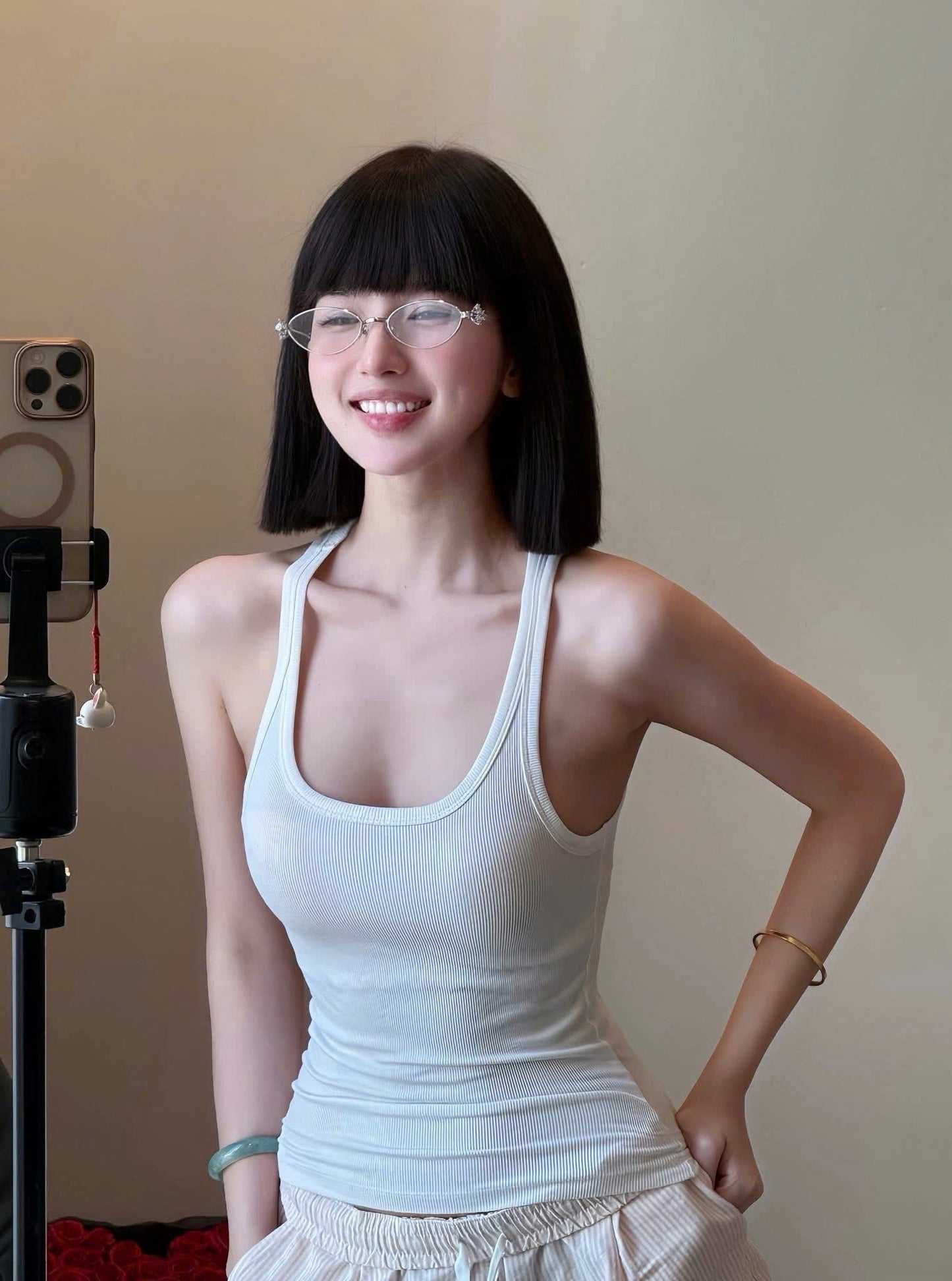 Woman wearing a white tank top and Gentle Monster (GM) Carat 02, standing next to a camera on a tripod.