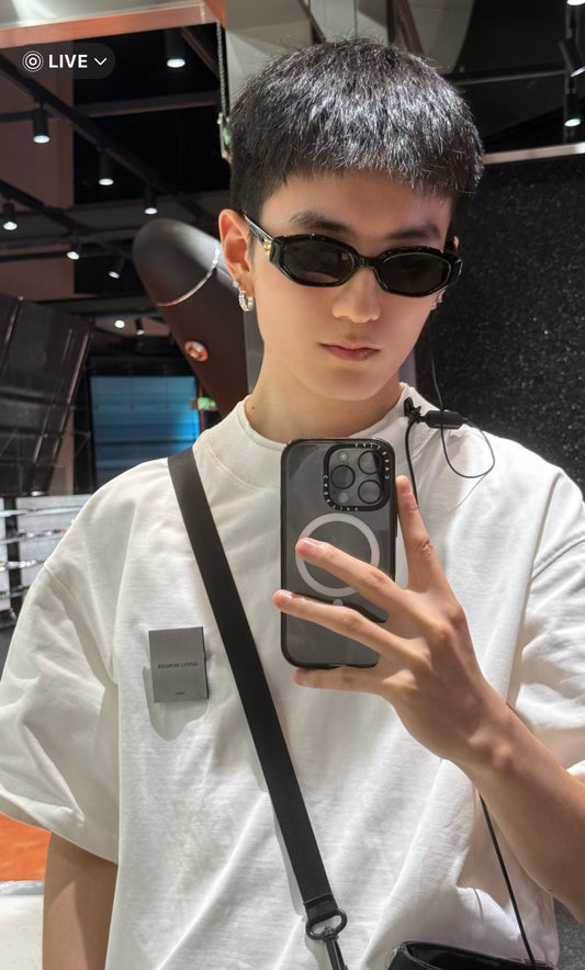 Person wearing Gentle Monster (GM) Miro 01 and a white shirt, holding a phone with a crossbody bag.