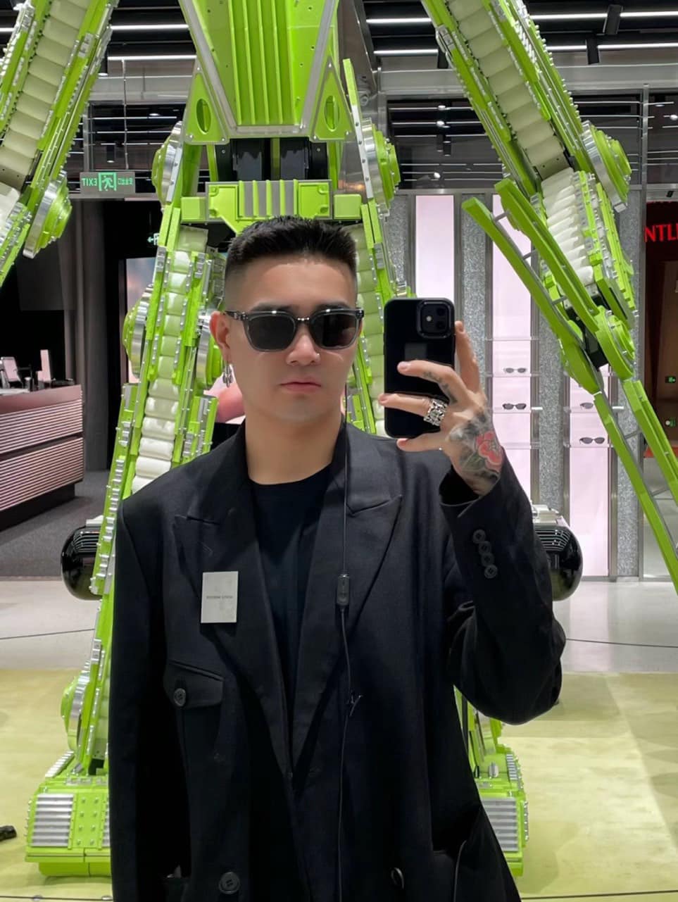 Person with Gentle Monster (GM) Nubo G3 taking a selfie in front of a large green sculpture in an indoor setting