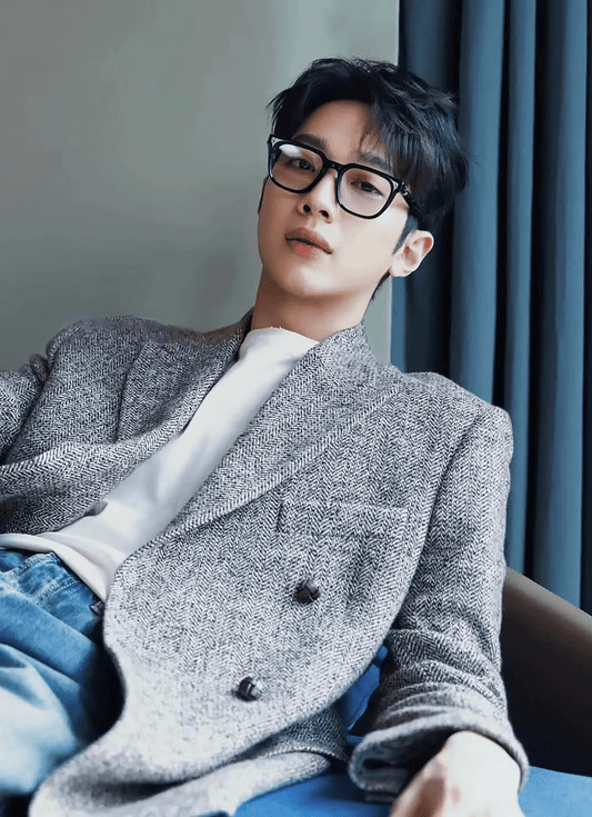 Person wearing a gray blazer and Gentle Monster (GM) Ojo 01, sitting indoors.