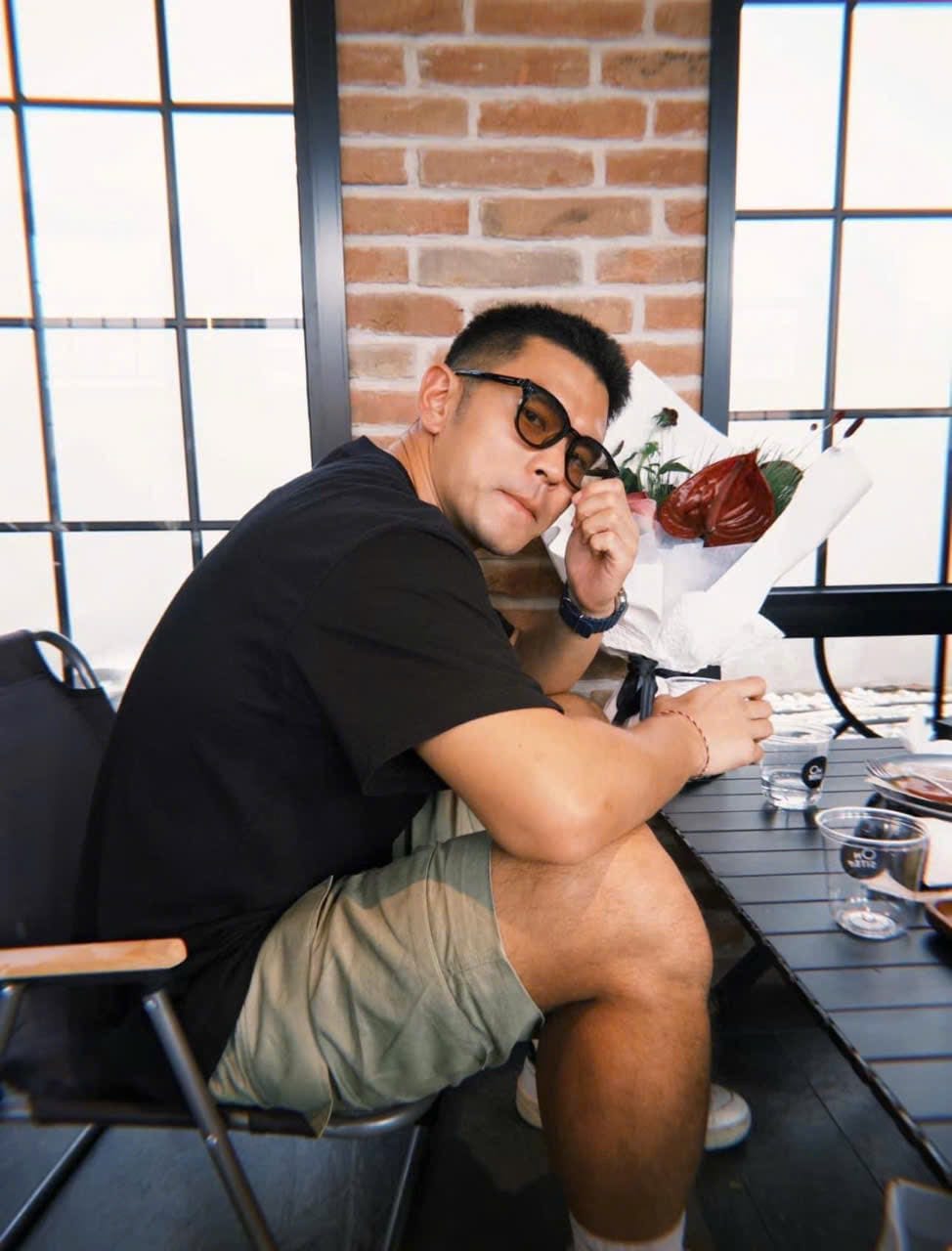 Man wearing Gentle Monster Jade 01(BR) Round Sunglasses & sitting at a table with a brick wall and large windows in the background