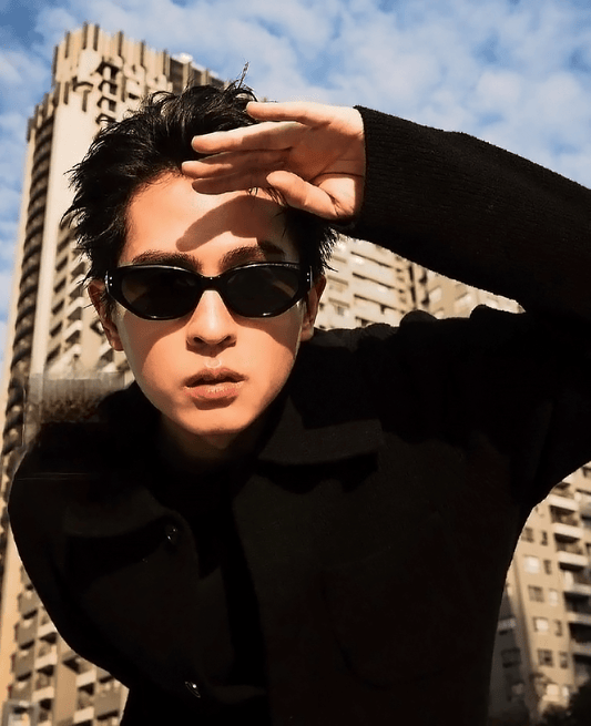 Person wearing Gentle Monster (GM) Rococo 01 and a black coat with a cityscape background