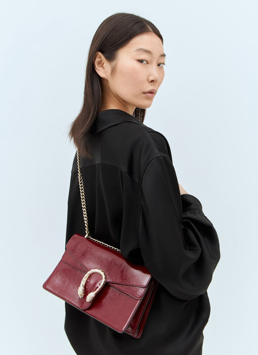 Woman carrying a Gucci Dionysus Medium Shoulder Bag Rosso Ancora 795005 0AAA8 6207 with a gold chain strap on a light blue background