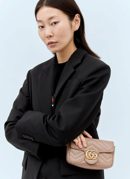 Woman holding a Gucci GG Marmont Matelassé Leather Mini Bag Dusty Pink 476433 DTDCT 5729 with a gold logo against a light blue background