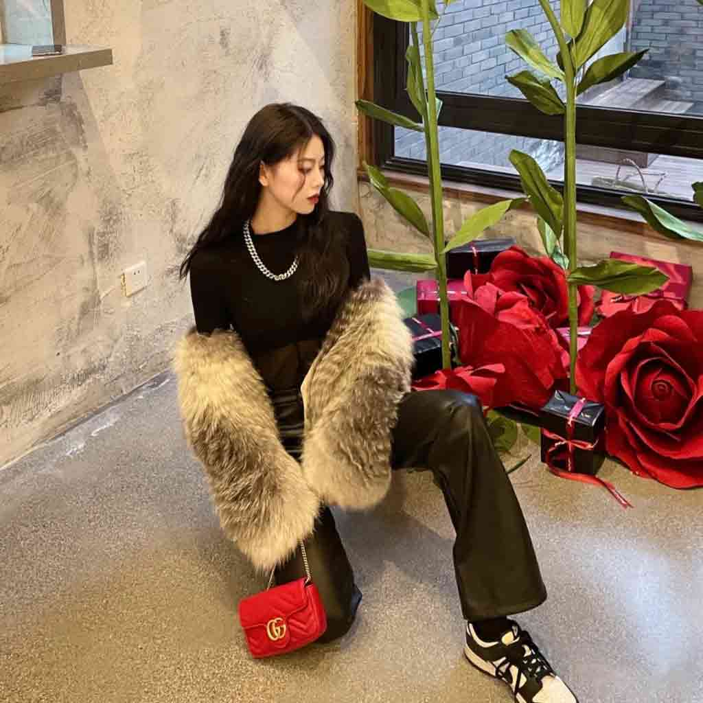 Woman sitting on a chair with a fur stole and Gucci GG Marmont Matelassé Mini Bag in Red Leather 476433 DTDHT 6832, surrounded by large red roses and gift boxes.