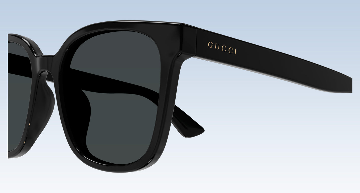 Gucci GG1346SK 001 Black Square Oversize Sunglasses with dark lenses and gold logo lettering on the temple, shown against a light blue gradient background.
