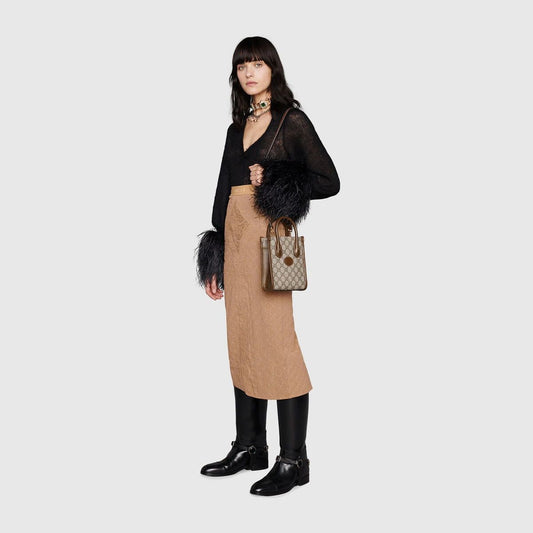 Woman wearing a black sheer top, beige skirt, and black boots with a Gucci Interlocking G Mini Tote Bag 671623 92TCG 8563 on a white background