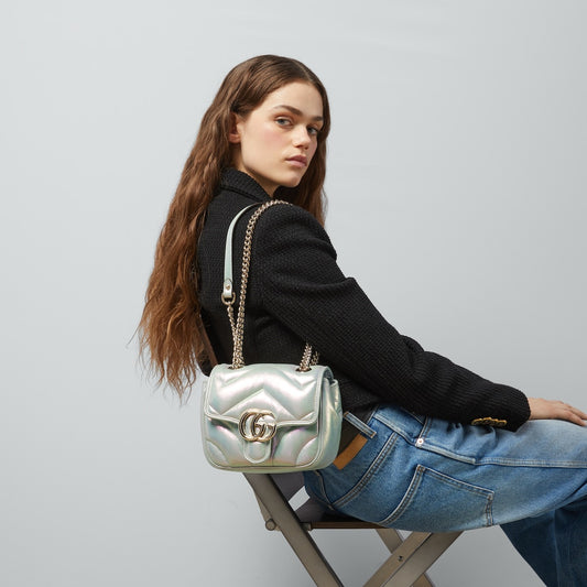 Woman holding a Gucci GG Marmont Iridescent Mini Crossbody Bag in Green 739682 AAC2U 3404 handbag against a plain background
