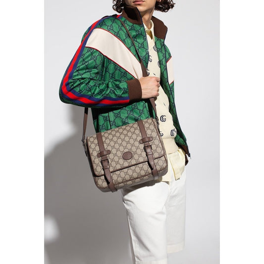 Person wearing a patterned jacket holding a Gucci Medium Messenger Interlocking GG Bag Supreme Beige Ebony 658542 K9GSN 8538 against a white background