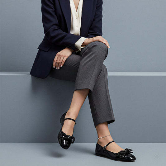 Person wearing a navy blazer, gray pants, and MACH & MACH Double Bow Black Patent Ballet Flat sitting on a gray surface.