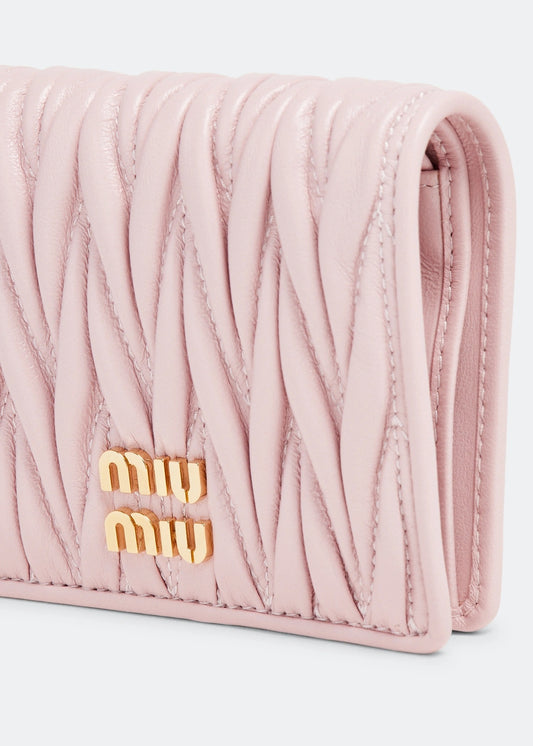 Pink quilted wallet with gold 'miu miu' logo on a light gray background