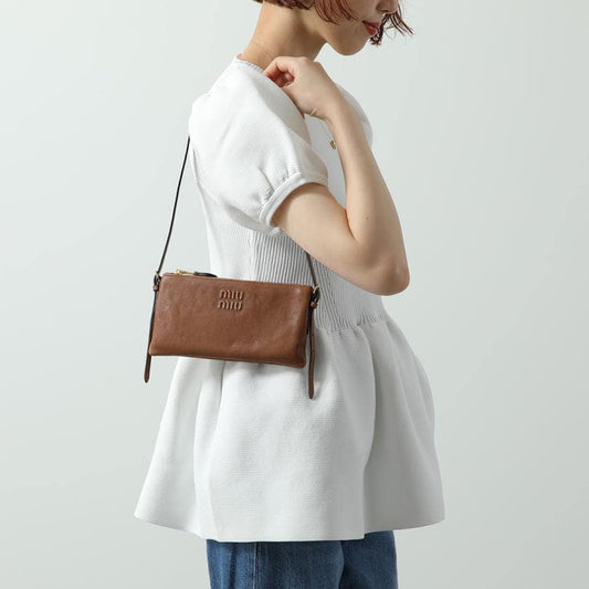 Person wearing a Miu Miu Oak Nappa Leather Mini Pouch 5NI007_AEFX_F0316 with 'miu miu' branding on a plain background
