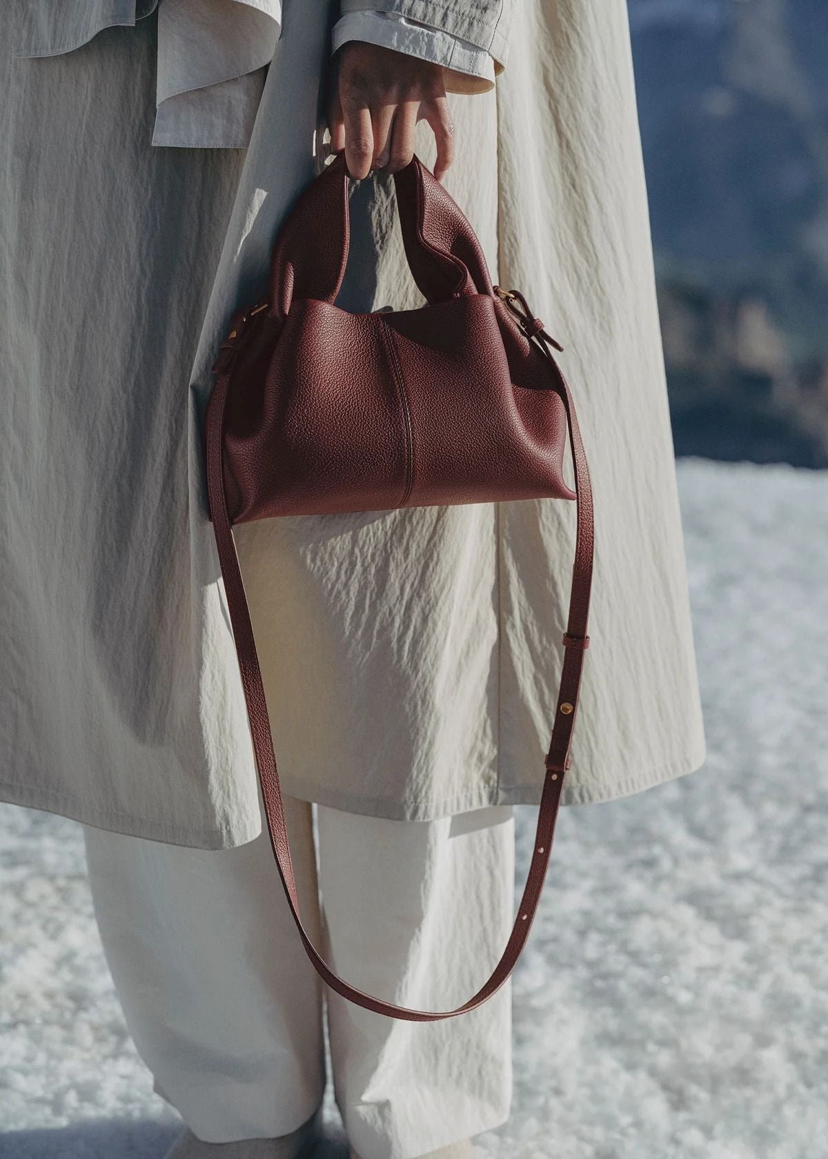 Person holding a Polène Numéro Neuf Mini Edition Textured Black Cherry with a blurred natural background