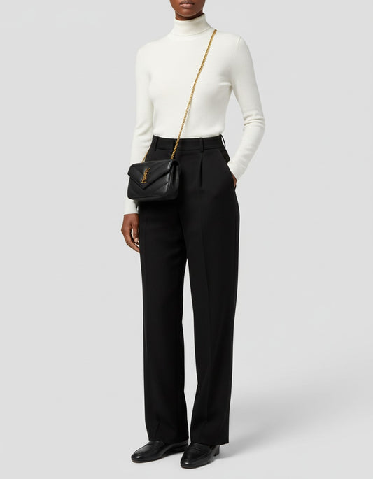 Person wearing a white turtleneck, black high-waisted pants, and black shoes with a Saint Laurent LOULOU MINI in Lambskin Black 821749AAEAX1000 on a light gray background.