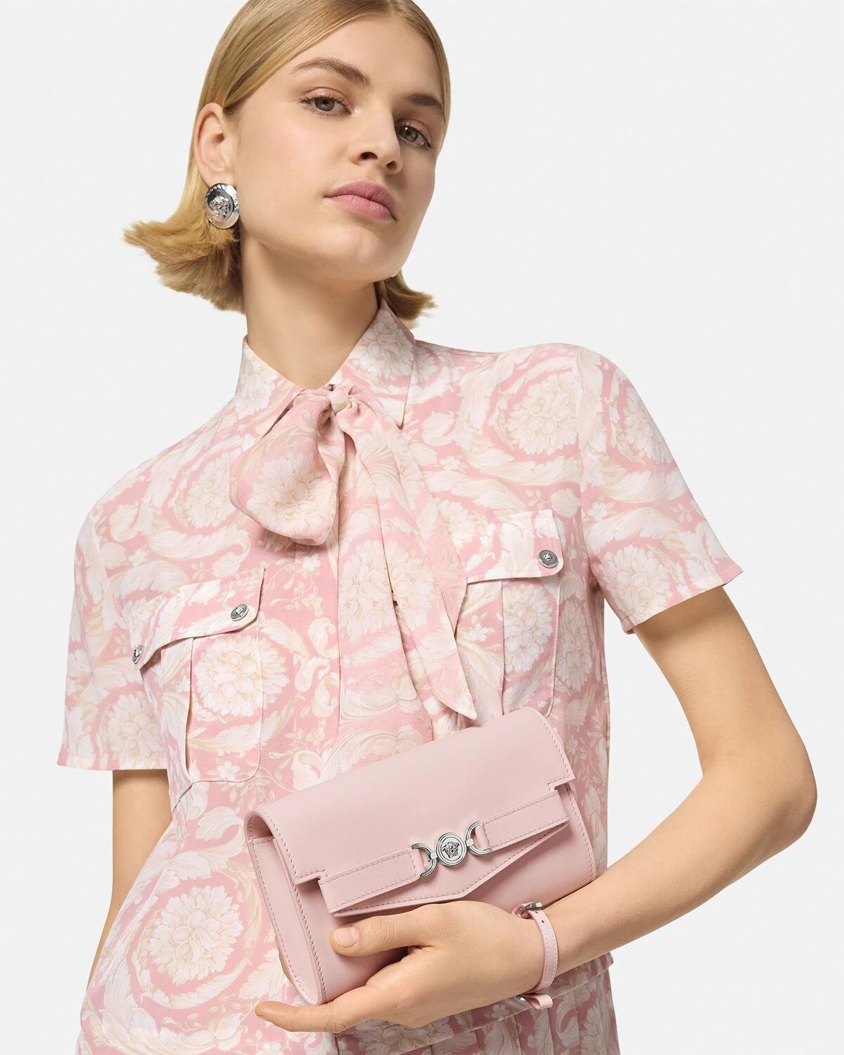 Woman holding a Versace Medusa '95 Crossbody Bag Light Pink 1014319 1A10795 1PT2P wearing a floral dress on a light gray background
