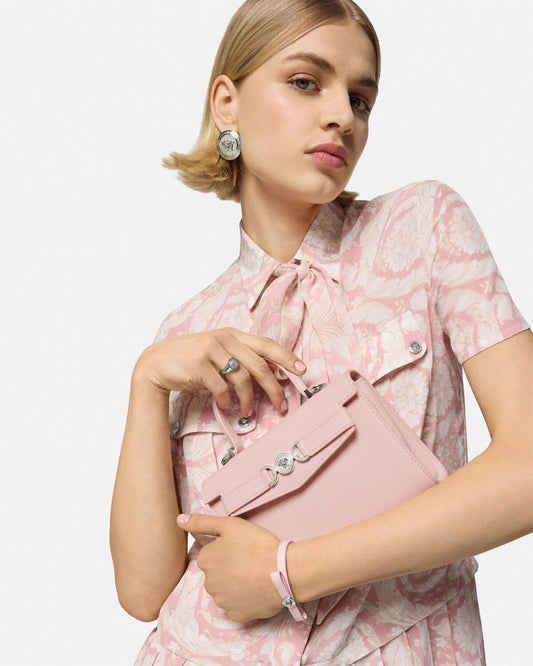 Woman holding a Versace Medusa '95 Small Handbag Light Pink 1013824 1A10795 1PT2P wearing a matching outfit against a light gray background