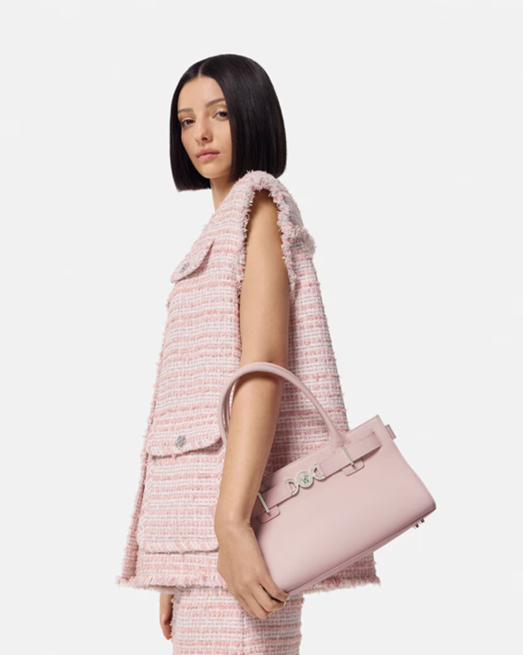 Woman holding a Versace Medusa '95 Tote Bag Light Pink 1013168-1A10795_1PT2P wearing a matching pink outfit on a white background