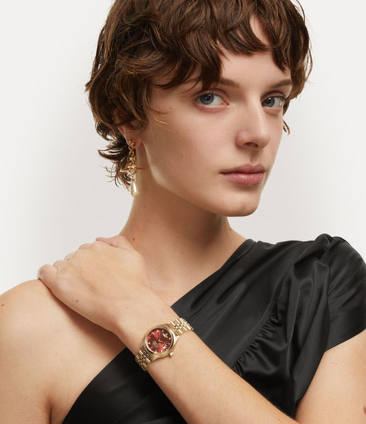 Woman wearing a Vivienne Westwood Little Camberwell Red Dial Gold Watch VV311RBGD 8050164230364 with a red gemstone on a plain background
