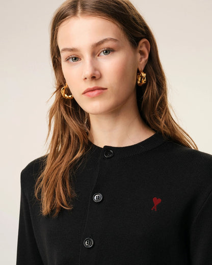 Woman wearing a black cardigan with a red heart emblem and gold earrings on a beige background