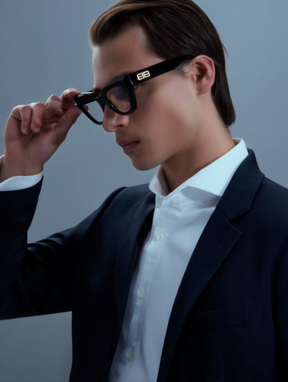 Man adjusting Balenciaga BB0238O-001 Butterfly Eyeglasses with a dark suit and white shirt against a gray background