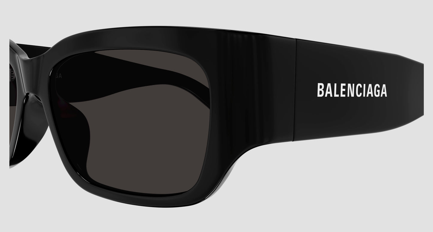 Black Balenciaga oversized sunglasses with dark lenses and the brand name printed in white on the temple, shown against a light gray background.
