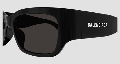 Black Balenciaga oversized sunglasses with dark lenses and the brand name printed in white on the temple, shown against a light gray background.