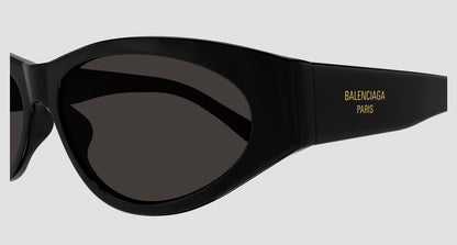 Close-up of a pair of Balenciaga BB0367S Round Sunglasses with a matte black frame and dark lenses, featuring gold 'BALENCIAGA PARIS' branding on the temple against a light gray background.