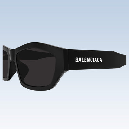 Balenciaga BB0448SK 001 Black Rectangular Sunglasses with a matte frame and dark lenses, featuring the white Balenciaga logo on the temple, set against a light blue gradient background.