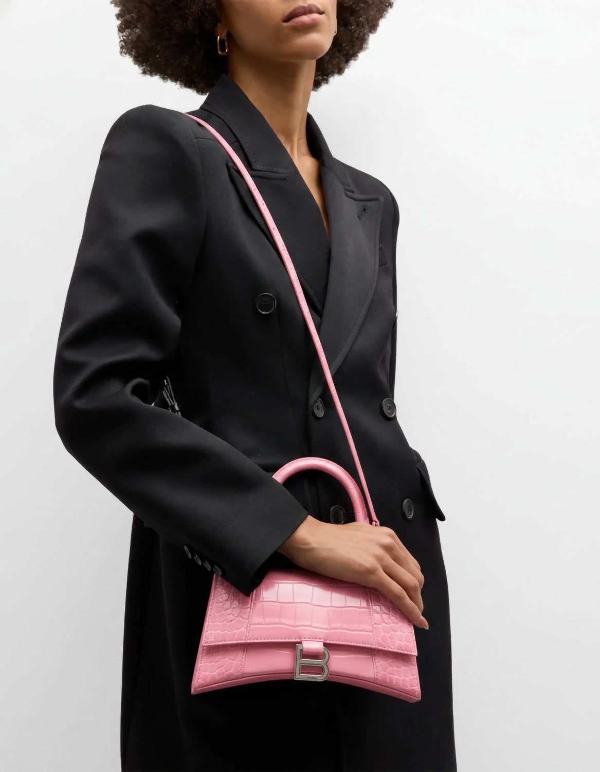 Person wearing a black coat hanging Balenciaga Hourglass Small Handbag – Crocodile Embossed Pink Calfskin 5935461LR6Y5812 against a white background