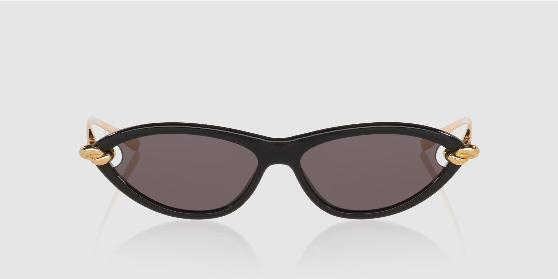 Bottega Veneta BV1390S Gold Knot Cat-Eye Sunglasses with dark lenses and gold metal accents on the temples, shown against a light gray background.