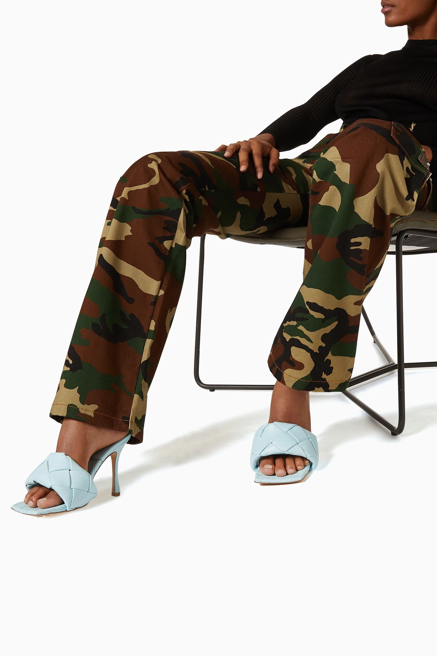 Person wearing camouflage pants and Bottega Veneta Lido Mule Pale Blue 608854VBSS04335 sitting on a chair.