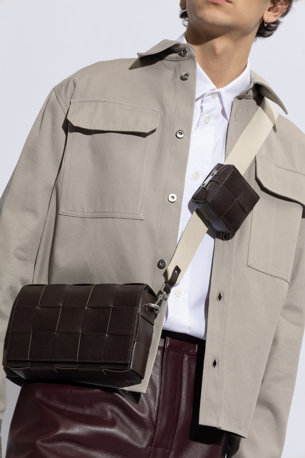 Person wearing a beige jacket with a Bottega Veneta Medium Brown Cassette Shoulder Bag With Versatile Strap 741777V2XU12094 over their shoulder against a light background