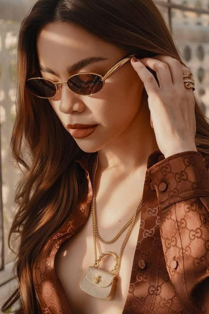 Hồ Ngọc Hà wearing Bottega Veneta Sardine BV1386S-001 Grey Gold Sunglasses 821495V44508043 and a patterned jacket with a handbag, outdoors.