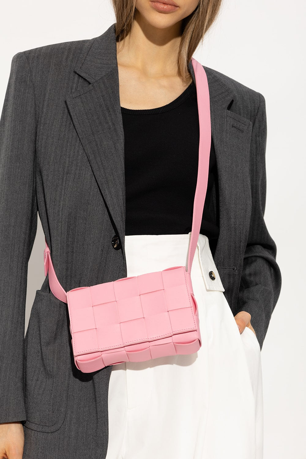 Person wearing a gray blazer and black top with a Bottega Veneta Small Cassette Shoulder Bag Pink 578004VMAY15832 on a white background