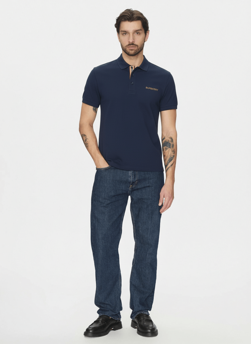 Man wearing a Burberry Hartford Polo In Navy 8084437 and blue jeans on a white background