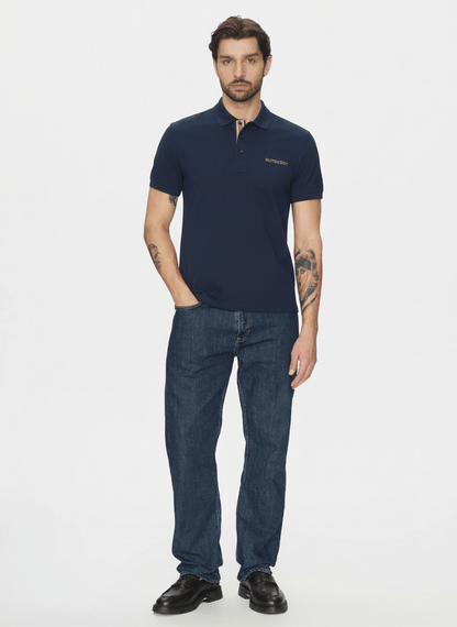 Man wearing a Burberry Hartford Polo In Navy 8084437 and blue jeans on a white background