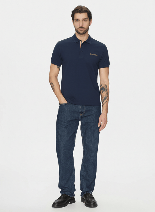Man wearing a Burberry Hartford Polo In Navy 8084437 and blue jeans on a white background