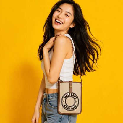 Woman holding a Burberry Logo Graphic Canvas Phone Pouch against a yellow background