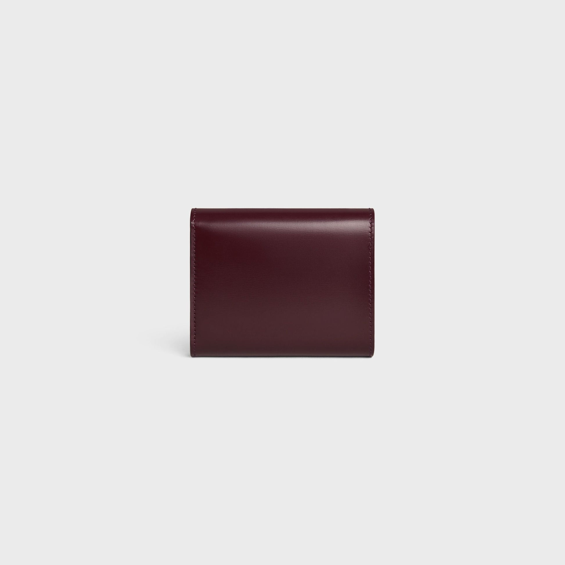 behind Celine Small Flap Wallet TRIOMPHE in Shiny Calfskin Deep Burgundy / Silver 10D783DPV.28DC on a light gray background