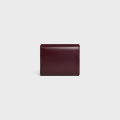 behind Celine Small Flap Wallet TRIOMPHE in Shiny Calfskin Deep Burgundy / Silver 10D783DPV.28DC on a light gray background